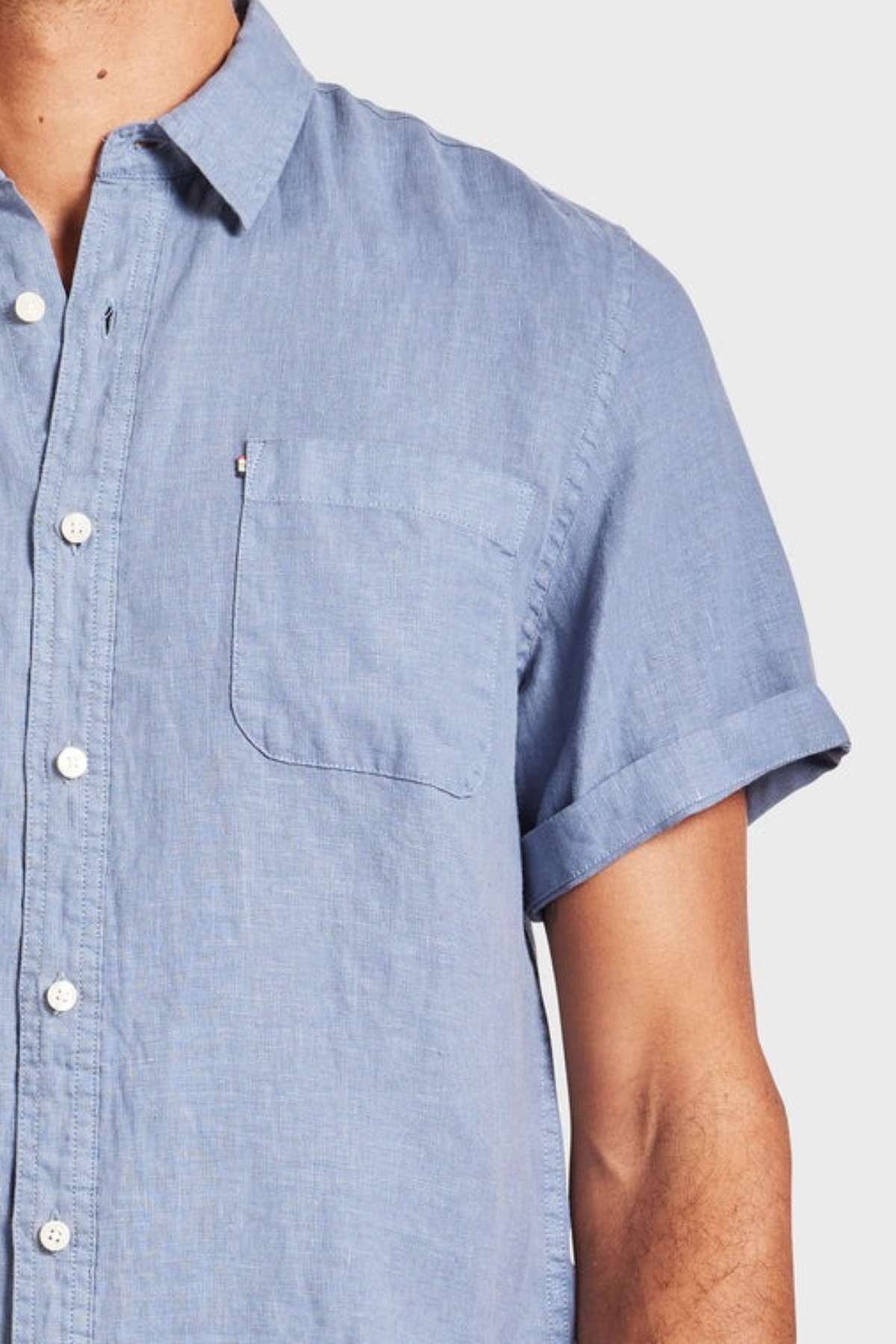 A person wears the Academy Brand Hampton Linen Short Sleeve Shirt in light blue, showcasing its chest pocket and short sleeves. Only the upper torso and part of one arm are visible against a plain background.
