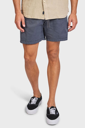 Wearing a beige shirt, black-and-white sneakers, and Academy Brand Oahu Short, a person stands against a plain white background. The image is cropped from the shoulders down to highlight the vintage charm of their outfit.