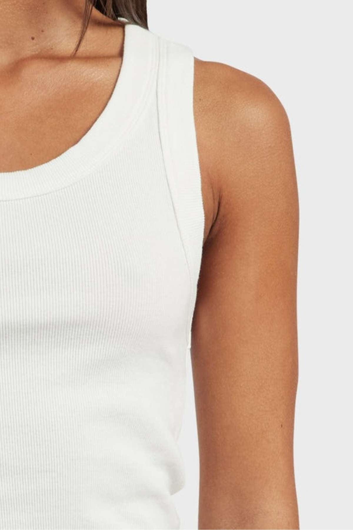 Close-up of a person wearing the Academy Women Essential Rib Tank. The image emphasizes the upper left portion of their torso, showcasing the premium, garment-washed rib texture against their natural skin tone. This essential piece, with its versatile design, is perfect for any summer wardrobe, set against a solid light gray background.