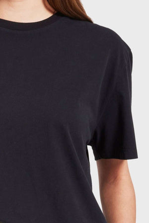 Close-up of a person wearing a plain black Academy Women Jimmy Boyfriend Tee, showing the shoulder and part of the arm against a plain, light background. The premium sanded jersey T-shirt has a casual, relaxed fit, and the person's hair is partially visible.