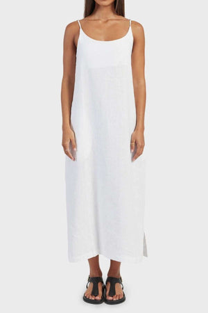 A person in a simple, sleeveless Academy Women Essential Linen Slip Dress with thin straps and black sandals stands against a plain white background. This ankle-length dress is the perfect addition to any summer wardrobe.