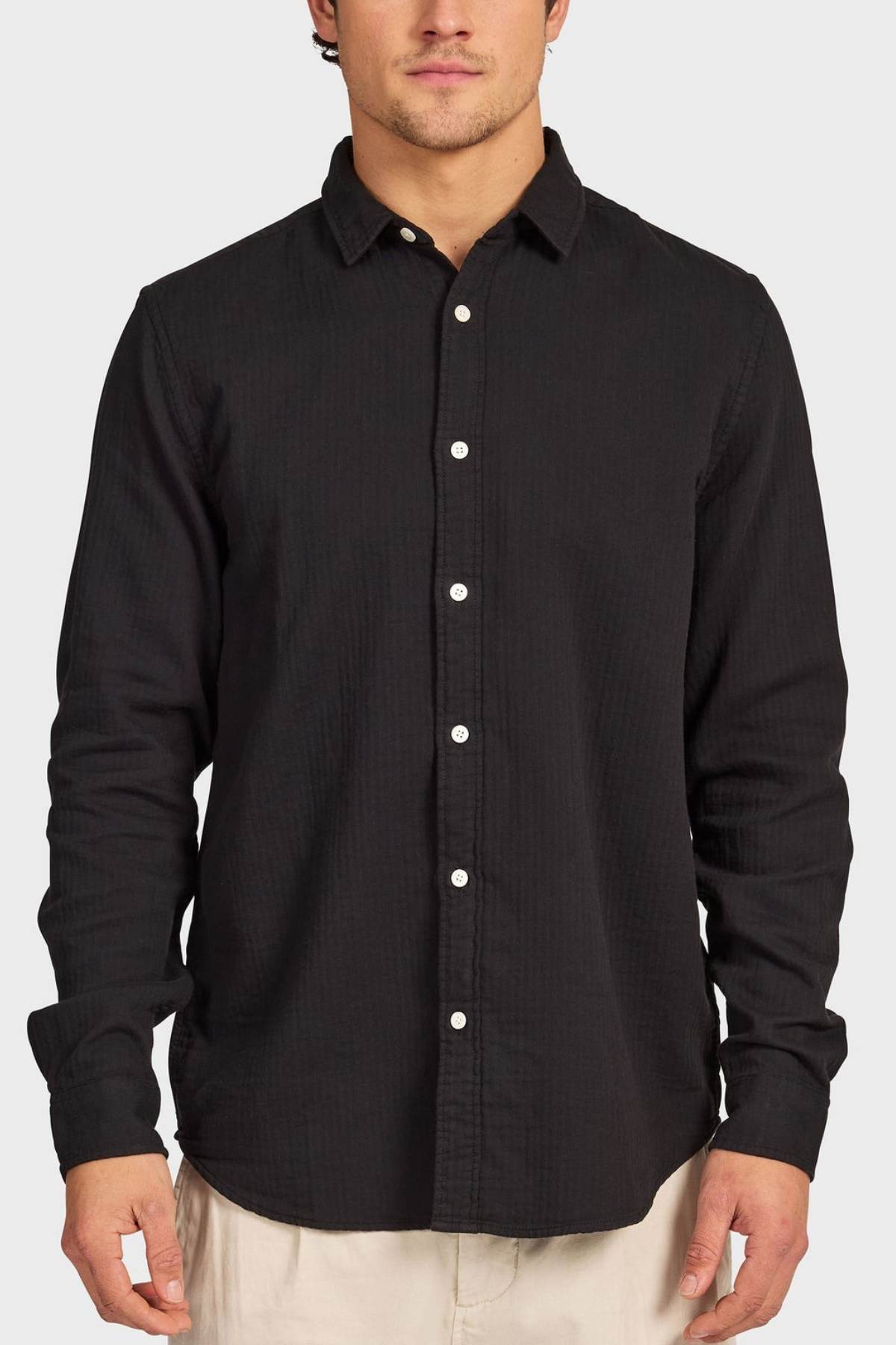 A man wears the Academy Brand Harry Double Cloth Shirt—a long-sleeve cotton shirt with white buttons and beige pants—standing against a plain light gray background.