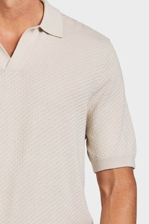 A man wears the Academy Brand Jonny Textured Knit Polo, featuring short sleeves and an ivory collar, shown from shoulders to mid-torso.