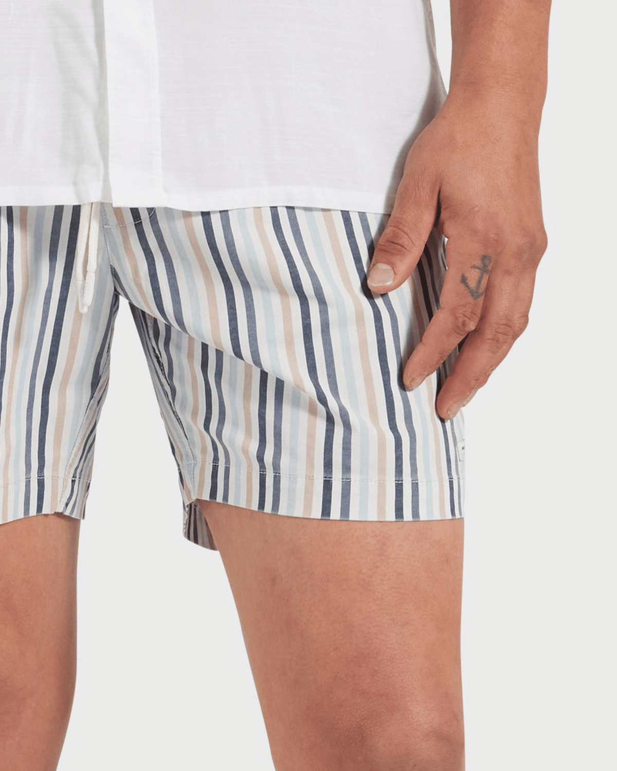 Wearing an Academy Brand Teamster Stripe Boardy in shades of blue, beige, and white, a person dons quick-drying striped shorts. An anchor tattoo on their hand complements the vintage vibe as they stand against a plain background.