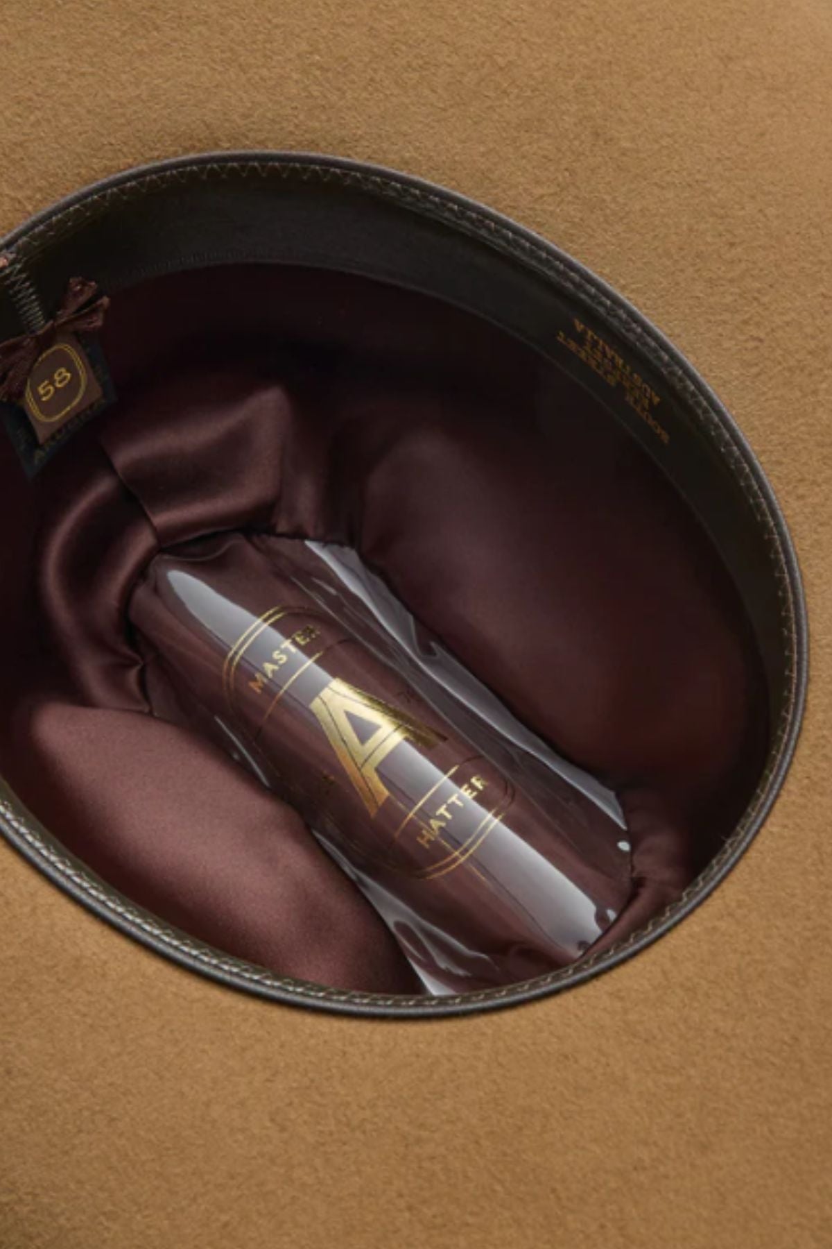 The Akubra Rough Rider is a brown felt hat with a satin-lined interior, presented in a clear cylindrical case marked with a gold "A" and "Master Hatter." A size 59 label highlights its classic, durable construction.