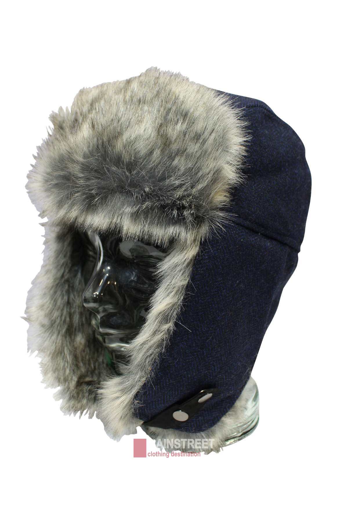 The Avenel Wool Blend Herringbone Flying Cap, a blue winter trapper hat, is displayed on a clear mannequin head. It has gray faux fur lining with buttoned ear flaps and a front flap for extra warmth.