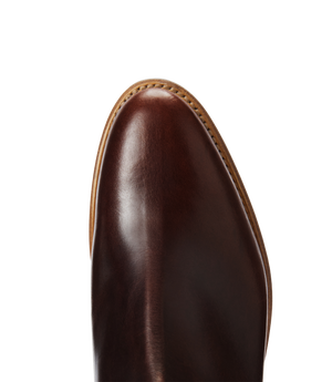 Close-up of the toe of the RM Williams Moriarty Rubber Sole Boot, featuring polished brown pull-up leather with visible stitching along the tan sole, set against a white background.
