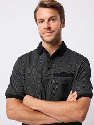 A light-haired man with a short beard stands against a plain background, arms crossed and smiling slightly, wearing the Breakaway Rafael Micro Prima Polo.