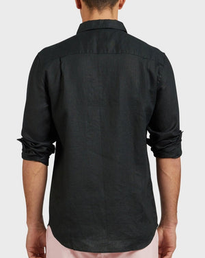 A man is seen from the back wearing the Academy Brand Hampton Linen Shirt in black with long sleeves partly rolled up, featuring a classic point collar. He pairs it with light-colored pants, standing against a plain light gray background.