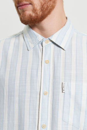 A man with a reddish beard wears a Ben Sherman Framed Candy Stripe Short Sleeve Shirt, light blue and white with vertical stripes, a small white chest pocket tag, and is cropped at the mouth and upper chest.