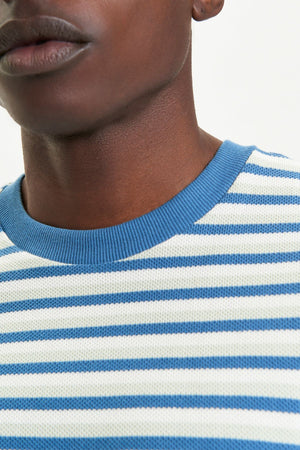 Close-up of a person in the Ben Sherman Honeycomb Stripe Tee, featuring blue and white stripes and a blue ribbed collar. Only the lower half of their face and neck are visible against a plain background.