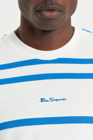 Close-up of a person wearing the Ben Sherman Mixed Stripe Tee, featuring blue horizontal stripes and "Ben Sherman" embroidery on the chest, made from soft pique cotton. The image highlights the lower face and upper torso.
