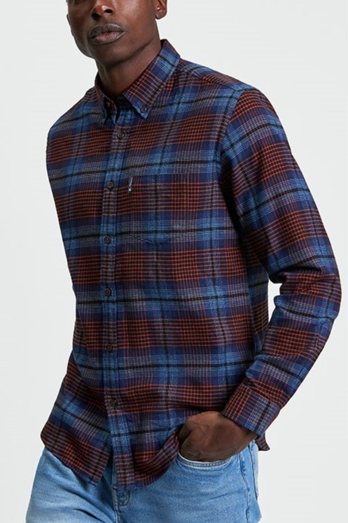 A person wears the Ben Sherman Ombre Check Shirt, a long-sleeve blue and red plaid button-up, paired with blue jeans. With one hand in their pocket, they stand against a plain light background.
