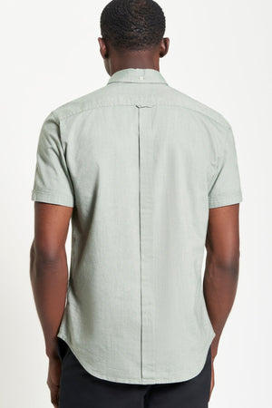 A man is seen from the back wearing the Ben Sherman Signature Oxford Short Sleeve Shirt in light green and black pants. The shirt features a small collar button, central back seam, and is shown against a plain white background.