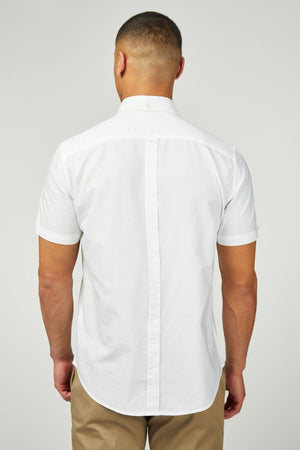 A man stands with his back to the camera, wearing a white Ben Sherman Signature Oxford Short Sleeve Shirt and tan pants, set against a plain light gray background.