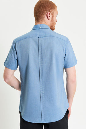 A man with short red hair, wearing a Ben Sherman Signature Oxford Short Sleeve Shirt in light blue and black pants, stands with his back to the camera against a plain white background.