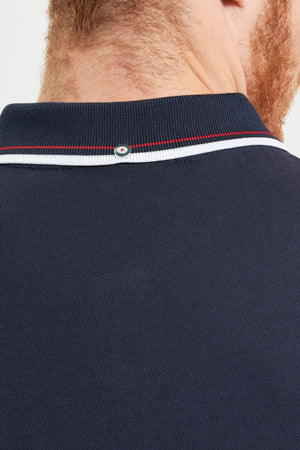 Close-up of the back of a person's neck and shoulders, wearing a Ben Sherman Signature Pique Polo in navy blue with white and red collar trim. The individual has light skin and a reddish beard.