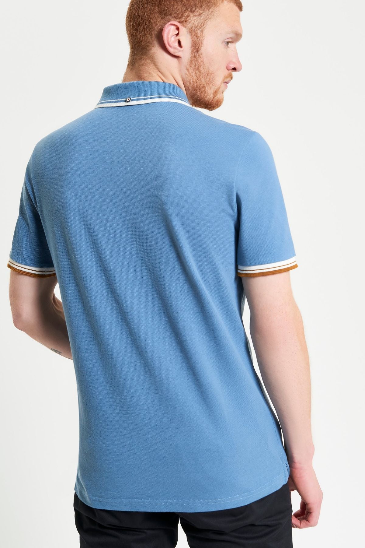A man with short red hair and a beard is shown from the back, wearing a light blue Ben Sherman Signature Pique Polo with white and brown sleeve trim and black pants, set against a plain white background.