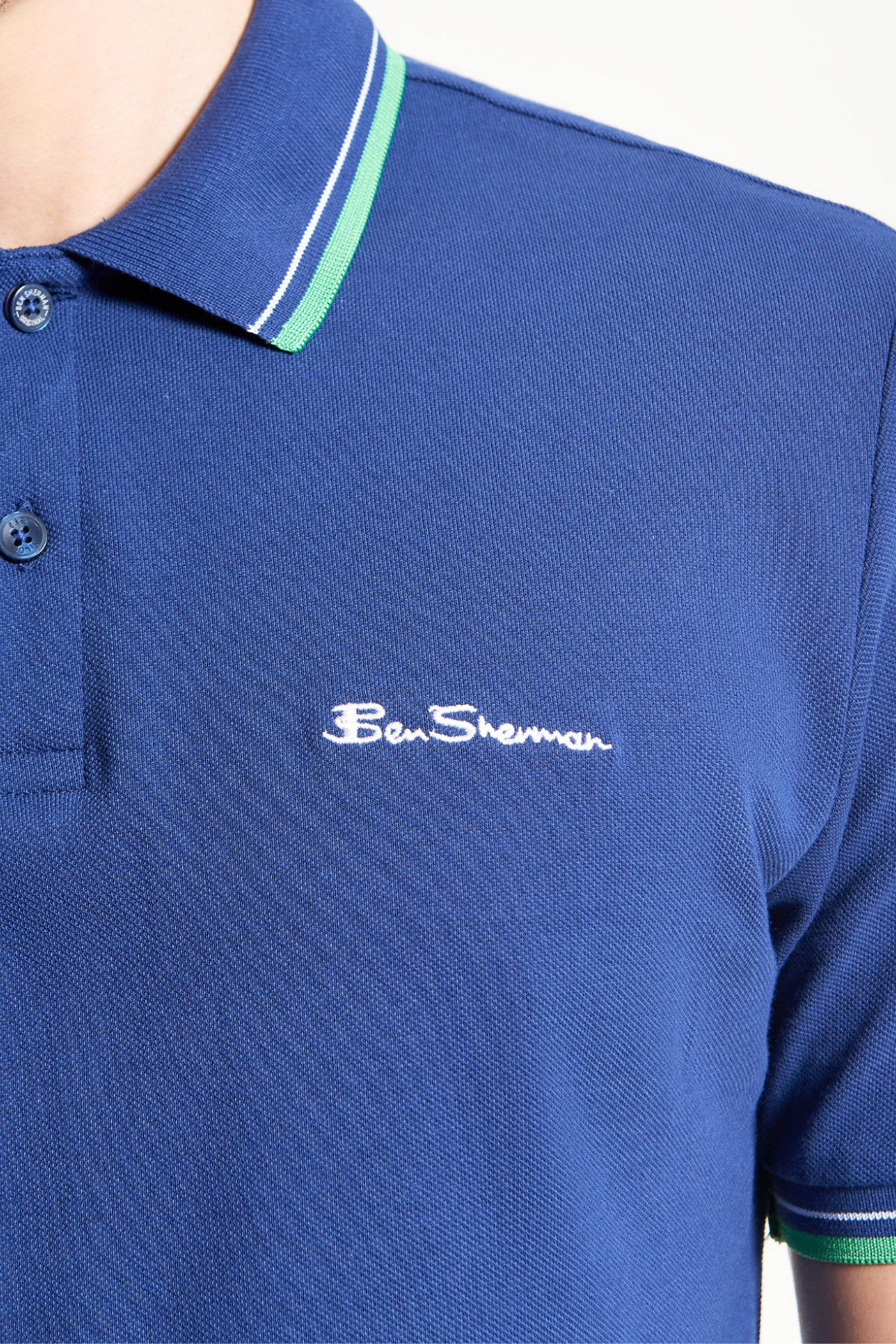 Close-up of a person wearing the Ben Sherman Signature Pique Polo in blue, showcasing green and white striped collar and the iconic white embroidered Ben Sherman logo on the chest.
