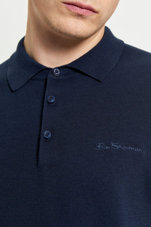 A close-up of a person wearing a dark navy Ben Sherman Signature Polo, featuring three buttons and subtle chest embroidery. The image focuses on the person's lower face and neck, showcasing this men's casual polo.