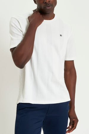 A man wears the Ben Sherman Textured Vertical Stripe Tee, made from 100% cotton with a small chest "B" logo, paired with navy pants and stands against a plain light background.