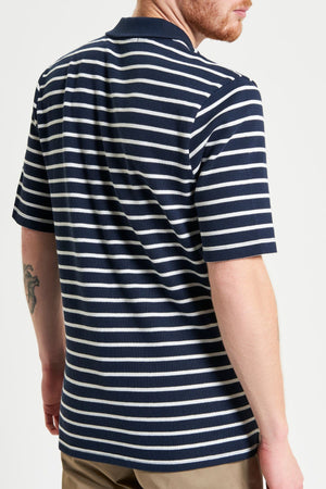 A man with a short beard, seen from the back, wears a Ben Sherman Waffle Stripe Polo in navy and white stripes with khaki pants. A tattoo is visible on his left arm.