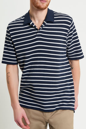 A person wearing the Ben Sherman Waffle Stripe Polo in navy blue and white horizontal stripes with beige pants, standing against a plain light background. Ideal for casual wear.