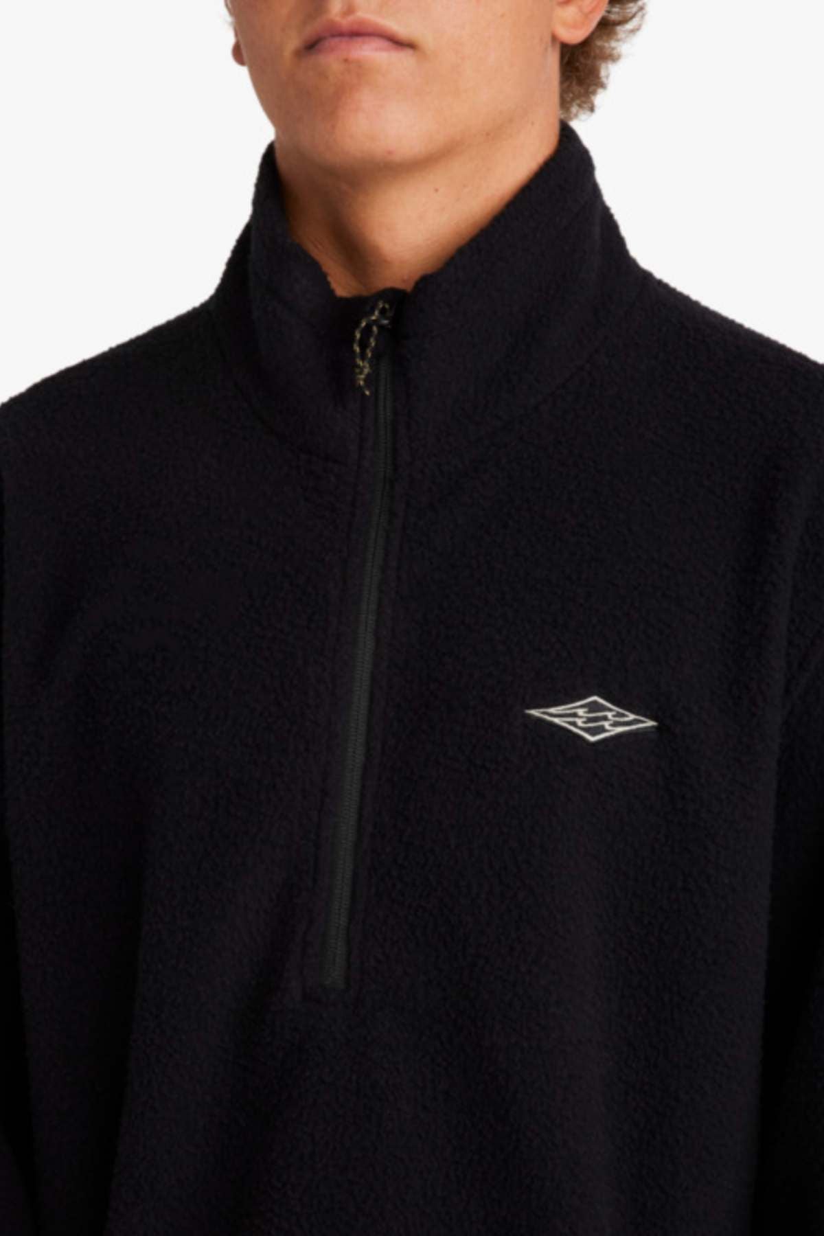 A person wearing a Billabong A/Div Boundary Mock Neck Sweatshirt, crafted from recycled polyester in black with a quarter zip and embroidered logo on the chest. The plain white background highlights its quality furnace fleece, ideal for Adventure Division activities.