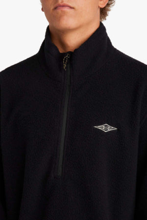 A person wearing a Billabong A/Div Boundary Mock Neck Sweatshirt, crafted from recycled polyester in black with a quarter zip and embroidered logo on the chest. The plain white background highlights its quality furnace fleece, ideal for Adventure Division activities.