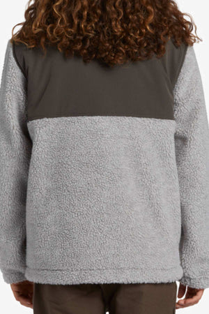 Person with curly hair shown from the back wearing the Billabong A/DIV Boundary Re-Issue Sweatshirt, made from recycled polyester with a light gray textured lower section and darker gray smooth upper sectionโperfect for outdoor adventures.