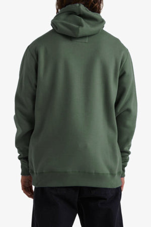 A person is seen from behind wearing a forest green Billabong Shoreline Pullover hoodie with long sleeves, relaxed fit, and cozy fleece lining, paired with dark pants against a plain white background.