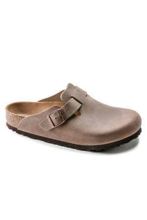 The Birkenstock Boston is a taupe leather clog featuring an open back, rounded toe, side buckle strap, anatomically shaped cork footbed, and textured dark sole.