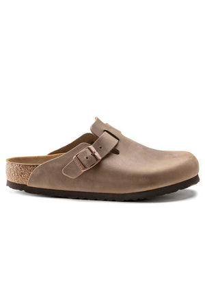 The Birkenstock Boston is a brown leather clog-style shoe with an anatomically shaped cork footbed, black sole, and an adjustable side buckle strap.