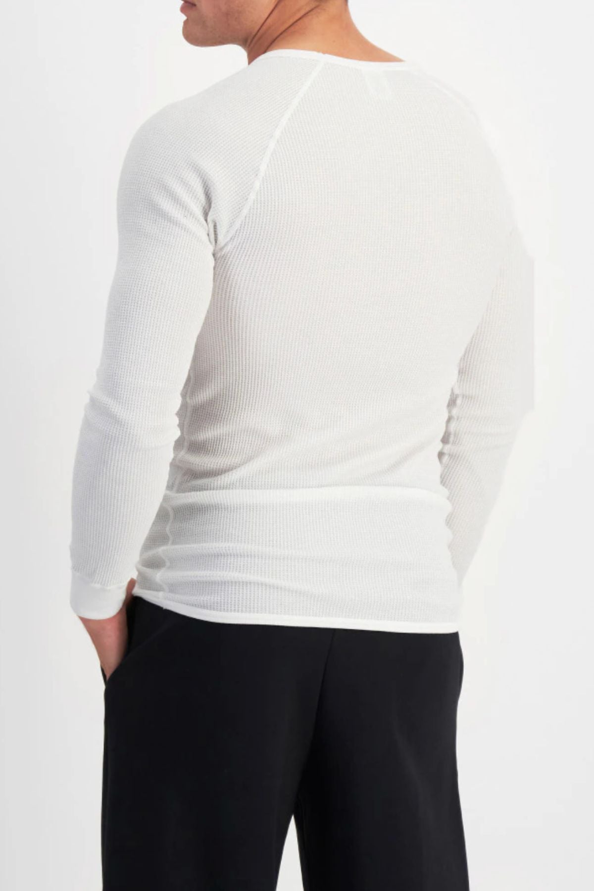 A person is shown from the back, hands in pockets, wearing the white Bonds Aircel Long Sleeve Tee and black pants against a plain white background.