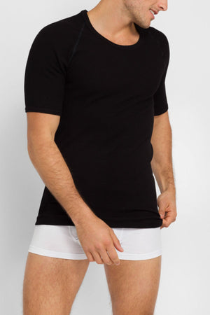 A man wearing a Bonds Aircel Short Sleeve Tee in black and white boxer briefs stands against a plain light background, looking to his right while slightly pulling down the hem of his shirt.