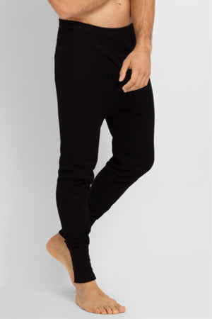 A man stands barefoot wearing Bonds Aircel Thermal Long Johns in black. The photo shows him from mid-chest down, one hand by his hip and the other arm relaxed.