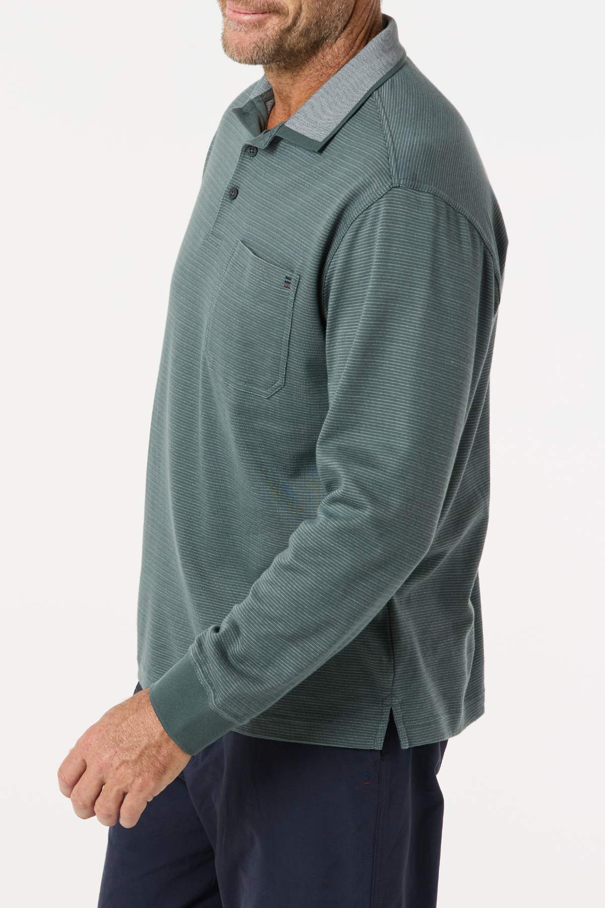 A man, face partially out of frame, stands against a white background wearing the Breakaway Avantee Micro Prima Polo in green with a chest pocket and rib knit cuffs, paired with navy pants.