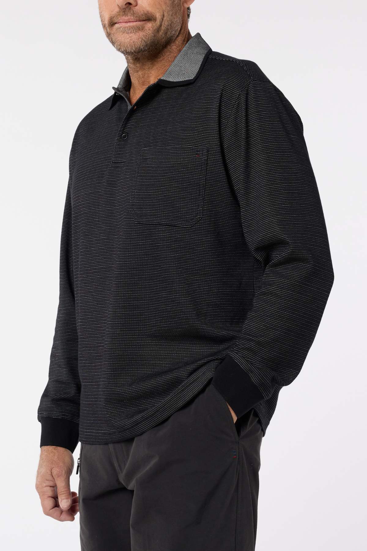 A man wears the Breakaway Avantee Micro Prima Poloβfeaturing a chest pocket, collar, and rib knit cuffsβstanding with one hand in his pocket against a plain background; a versatile wardrobe essential.