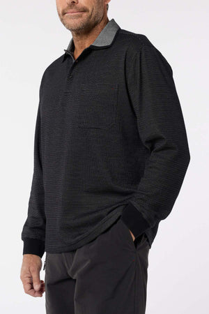 A man wears the Breakaway Avantee Micro Prima Poloβfeaturing a chest pocket, collar, and rib knit cuffsβstanding with one hand in his pocket against a plain background; a versatile wardrobe essential.