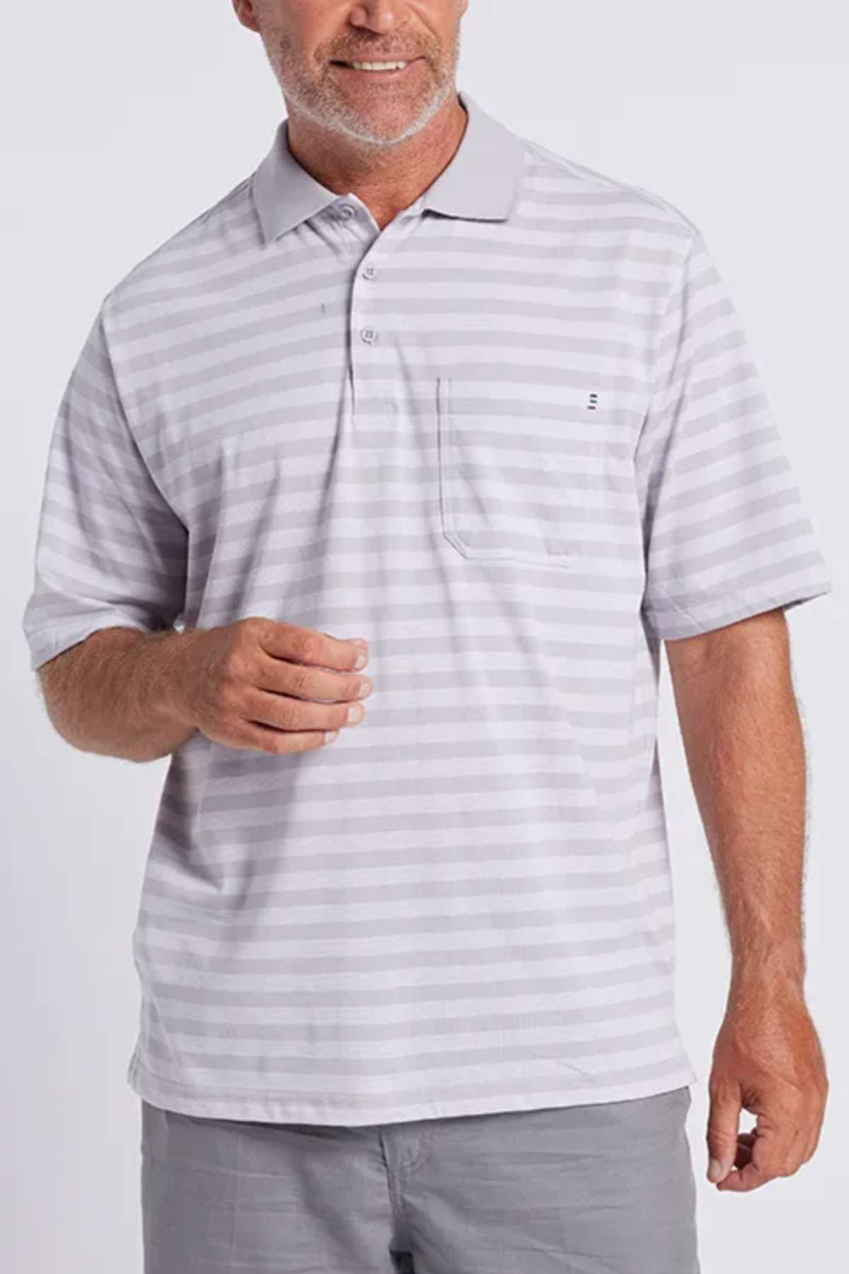A man with short gray hair and a gray beard is wearing the stylish and comfortable Breakaway Brady Kinnersly Polo, marked by its light gray and white stripe pattern, pocket on the left side, and contrast rib knit collar. He pairs it with gray pants as he stands against a plain background, smiling slightly.
