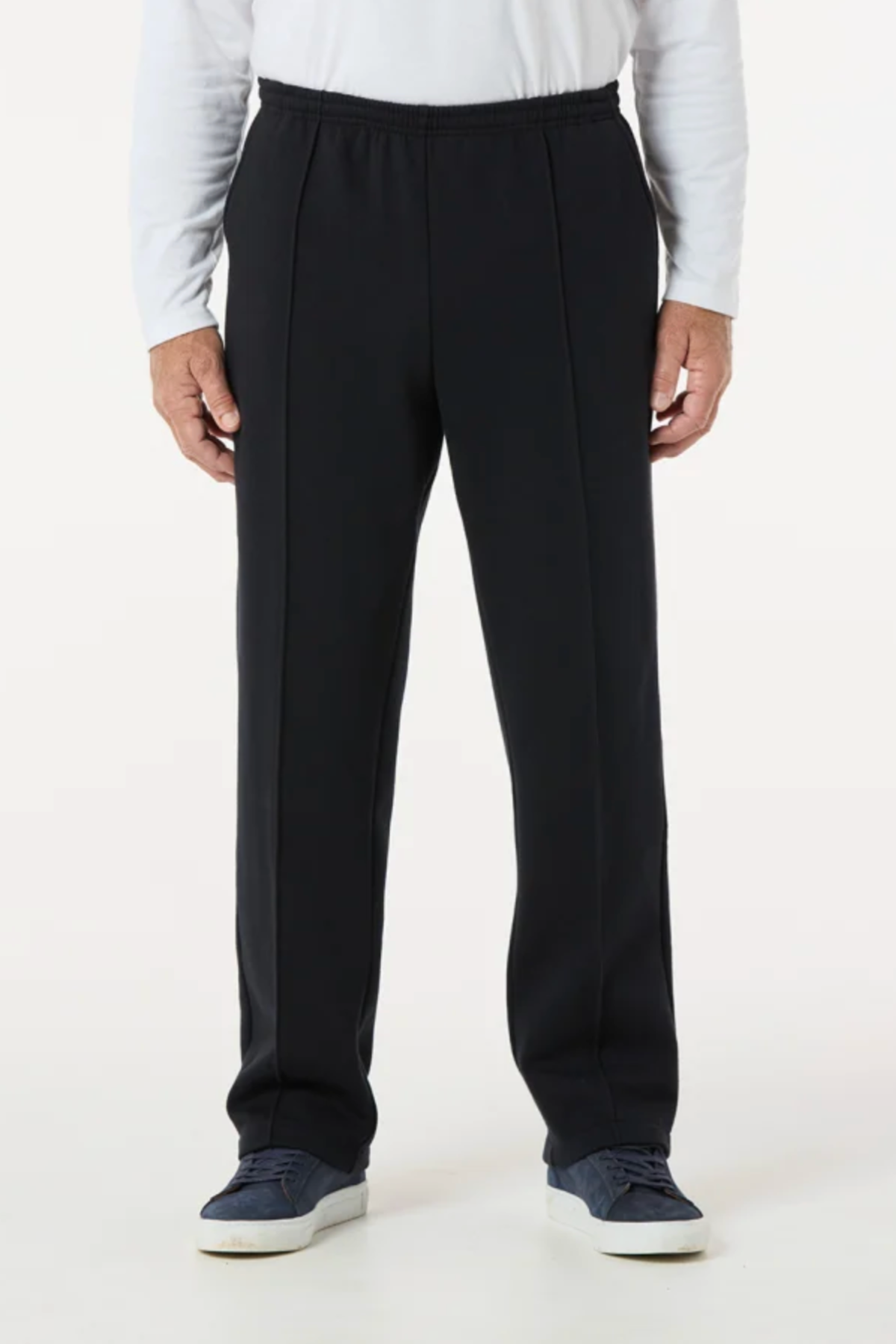Wearing Breakaway Classic Snowy Mt Fleece Pants with an elastic waist, a white long-sleeve shirt, and blue sneakers, this person poses against a plain white background in a relaxed, casual weekend look (image cropped from shoulders down).