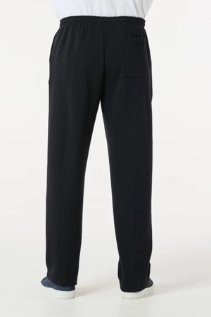 A person is seen from behind wearing Breakaway Classic Snowy Mt Fleece Pant—loose-fitting black pants with an elastic waistband and back pocket, straight to the ankles, styled casually with dark shoes.
