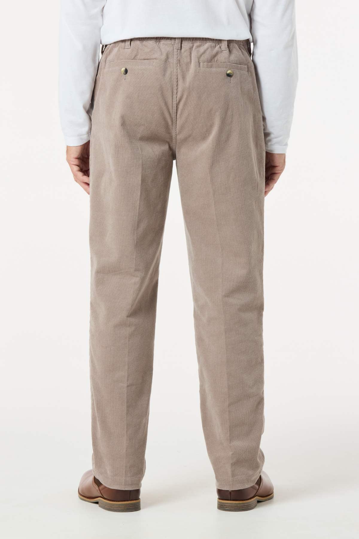 A person wearing light brown Breakaway Cordeaux Pants, brown shoes, and a white long-sleeve shirt stands with their back to the camera against a plain, light background.