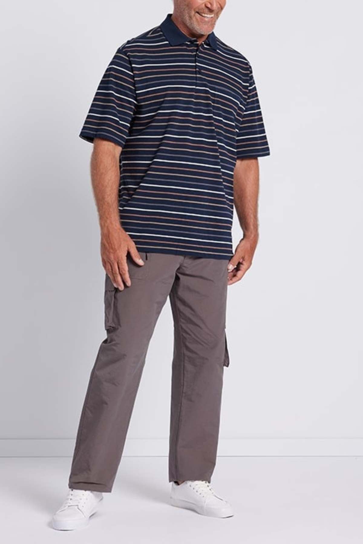 A man wearing a modern thin stripe navy blue and white Breakaway Dariyan Cotton Pique Polo, gray cargo pants, and white sneakers is standing and smiling against a plain white background.