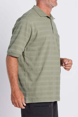 A person with short hair, dressed in a green Breakaway Emil Polo with self-jacquard stripes and black pants. Their face is turned slightly to the side, making it not visible, and they seem to be standing against a plain background.