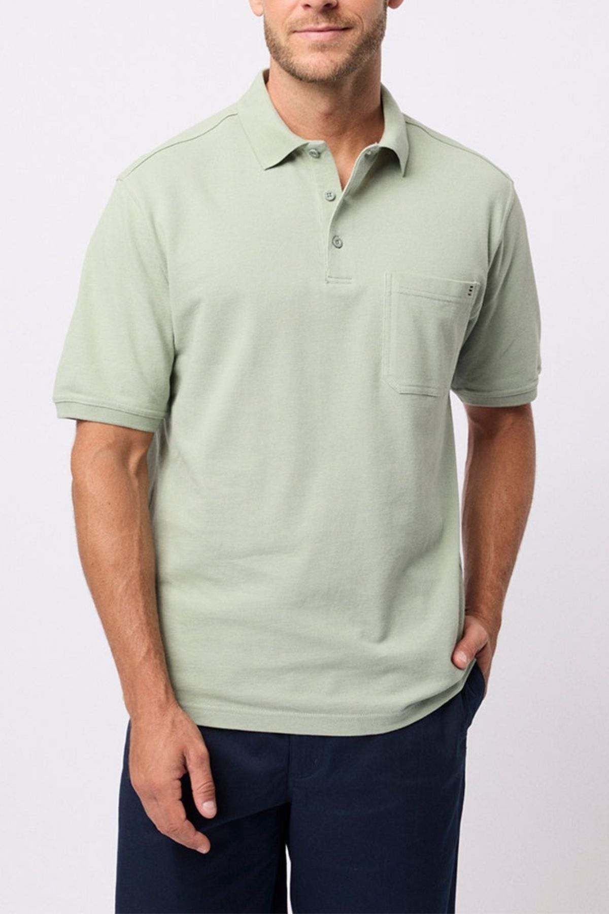 A man wears the Breakaway Fraser Cotton Pique Polo in light green with a chest pocket and dark blue pants, standing against a plain light background.