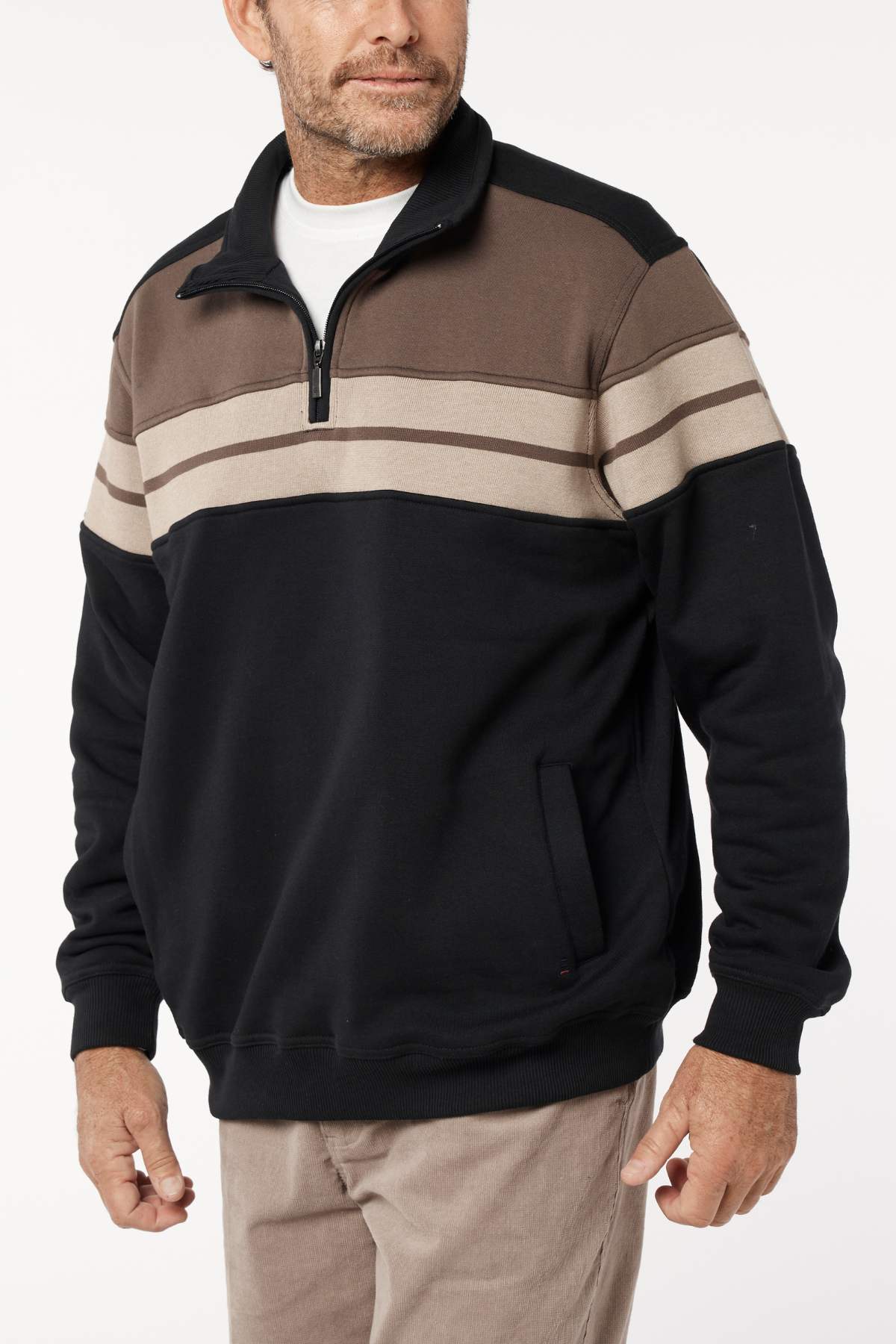 A man with short facial hair stands against a plain background wearing the Breakaway Henrich Snowy Mt Fleece Half Zip in black, brown, and beige with a wide stripe across the chest. He is looking to the side.