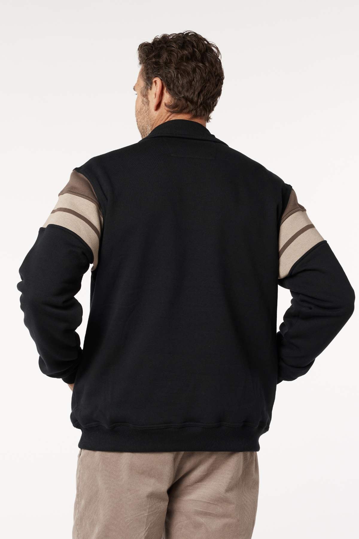 A man faces away from the camera, wearing a Breakaway Henrich Snowy Mt Fleece Half Zip with wide sleeve stripes and light pants, against a plain white background.