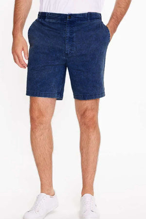 Against a plain white background, a person wears Breakaway Intense Denim Short in garment-dyed mid blue denim and white sneakers. The shorts feature side pockets, a fully elasticated waistband, and are above knee length. Only their lower half is visible.