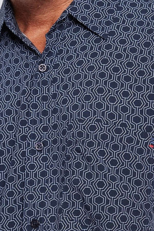 Close-up of an individual donning a navy blue Breakaway Jac Bamboo Shirt, adorned with a white geometric hexagonal pattern. The shirt features a partially visible front pocket and is worn with the top button undone. The person's face is not shown.